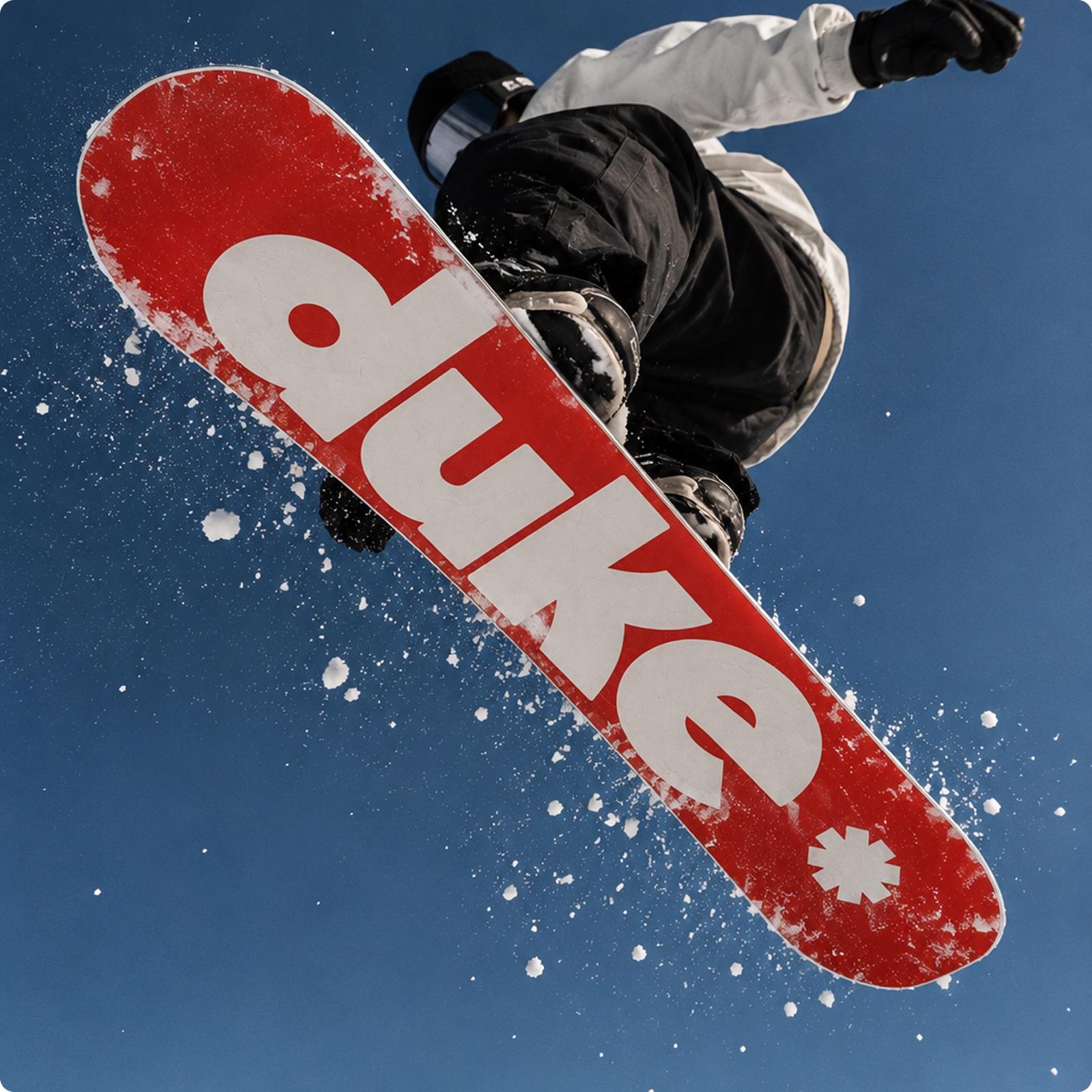 Snowboarder en el aire con una tabla roja con el logotipo de Duke