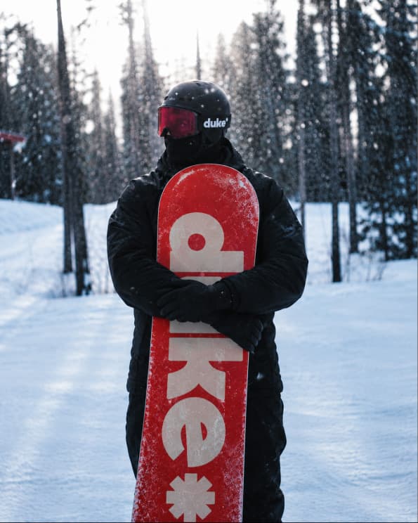 Snowboarder con una tabla roja de Duke en un bosque nevado