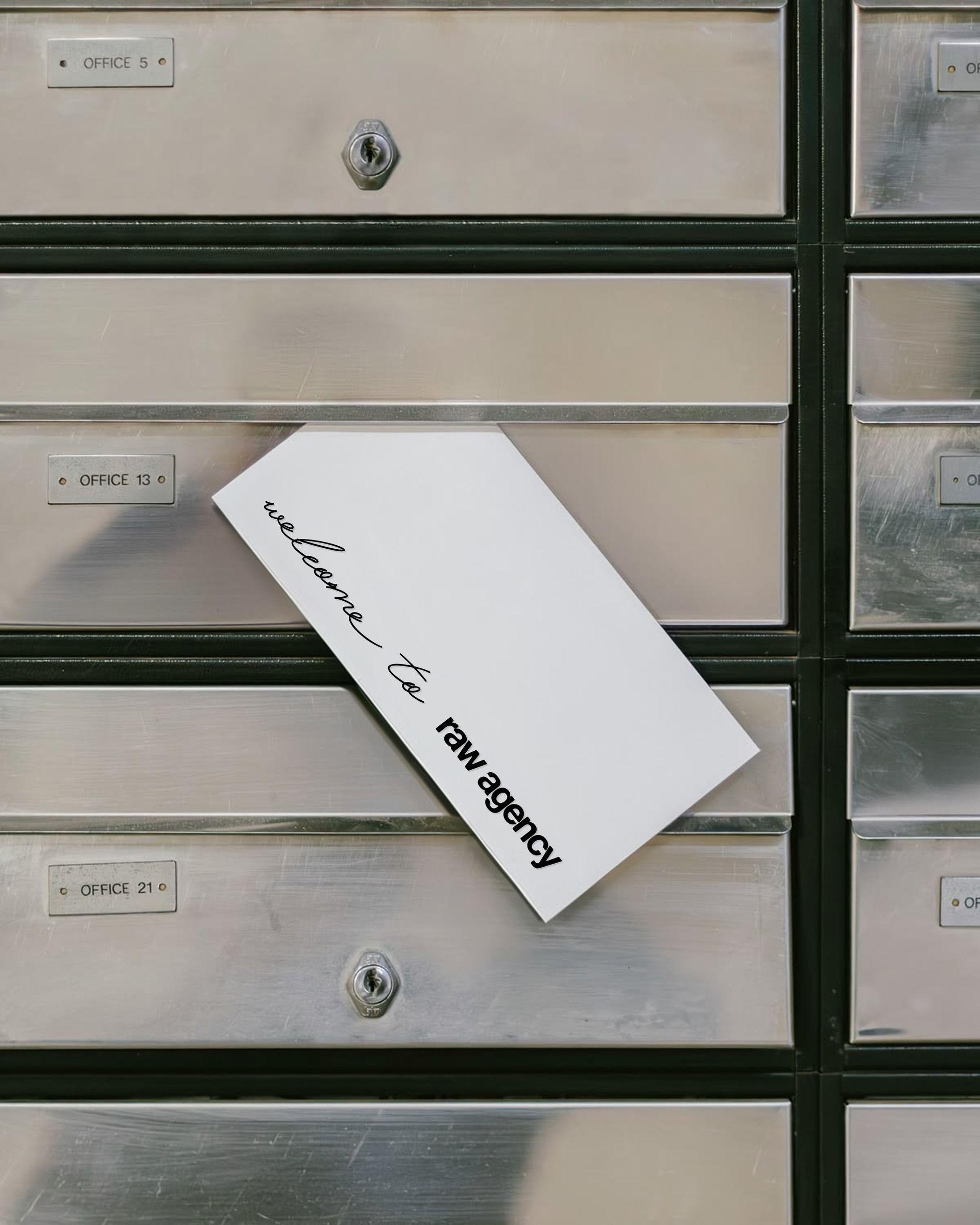 Tarjeta «welcome to raw agency» asomando de un buzón metálico de oficina